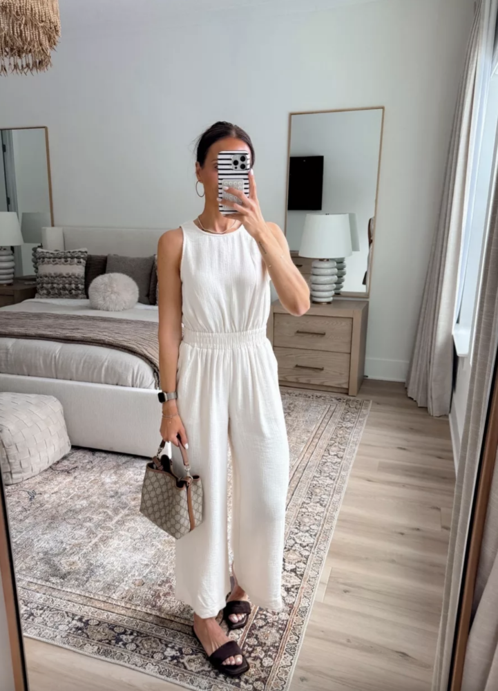 Women’s white sleeveless jumpsuit styled with a Gucci tote and black slide sandals, an easy and polished workwear outfit for summer to fall